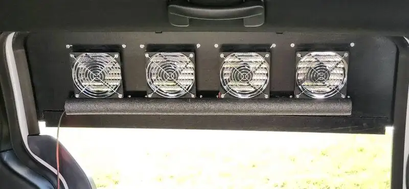 Interior view closeup of 12v fans used to push air through DIY window vents in a Dodge Grand Caravan, driver's side sliding door window.